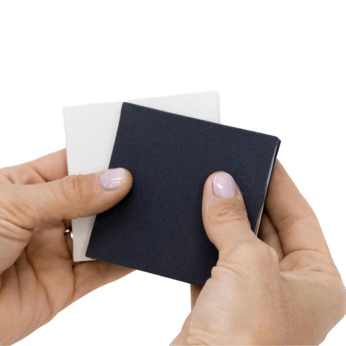 Fold, the accordion brag book, held in two hands, in cream and charcoal linen